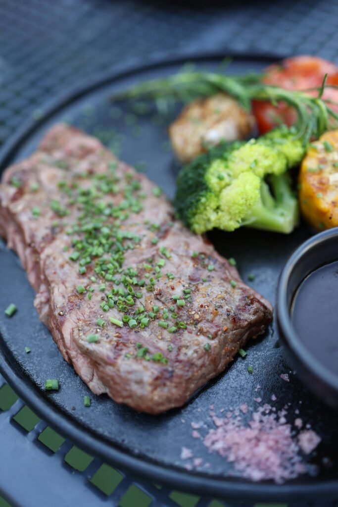 pexels-photo-25389777-25389777 A deliciously cooked steak topped with herbs, served with fresh vegetables on a black plate.