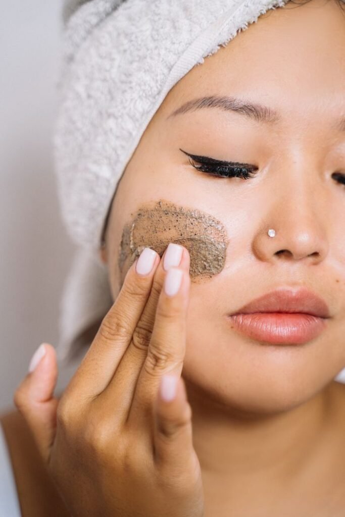 Close-up of woman applying facial scrub to cheeks, promoting skincare routine.